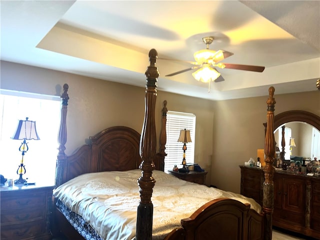 bedroom featuring multiple windows, ceiling fan, and a tray ceiling