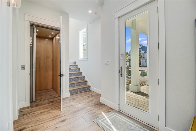 doorway featuring light wood finished floors, stairs, and baseboards