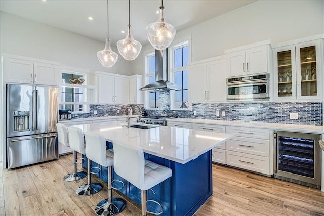 kitchen with wine cooler, light wood finished floors, appliances with stainless steel finishes, a sink, and wall chimney range hood