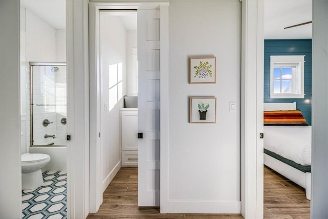 ensuite bathroom featuring baseboards, bath / shower combo with glass door, toilet, ensuite bath, and wood finished floors