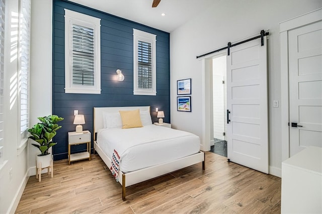 bedroom featuring a barn door, an accent wall, a ceiling fan, baseboards, and light wood-style floors