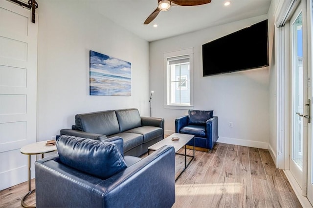 living area featuring ceiling fan, a barn door, wood finished floors, and baseboards