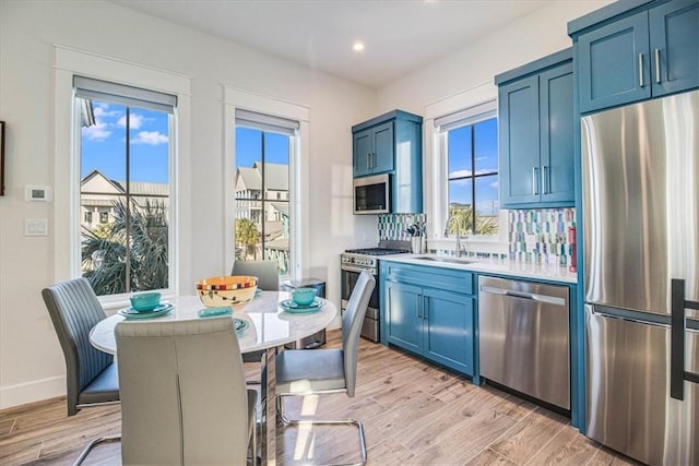 kitchen featuring stainless steel appliances, a sink, light wood-style flooring, and blue cabinets