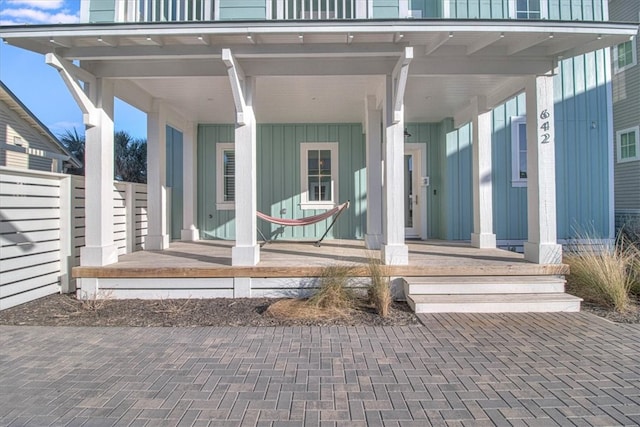 property entrance featuring covered porch, board and batten siding, and fence