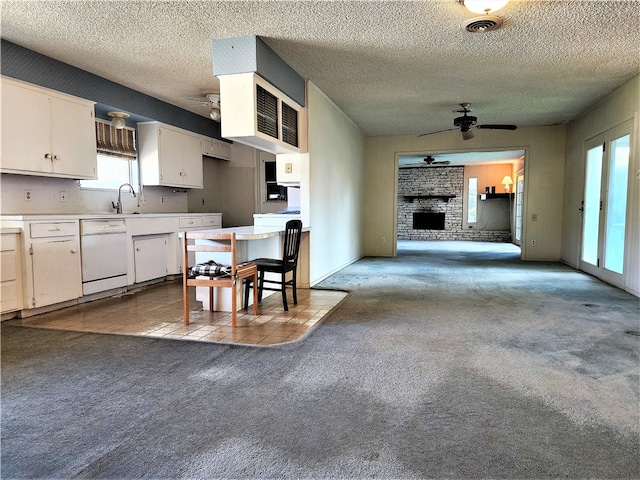 kitchen with ceiling fan, a textured ceiling, carpet floors, a brick fireplace, and dishwasher