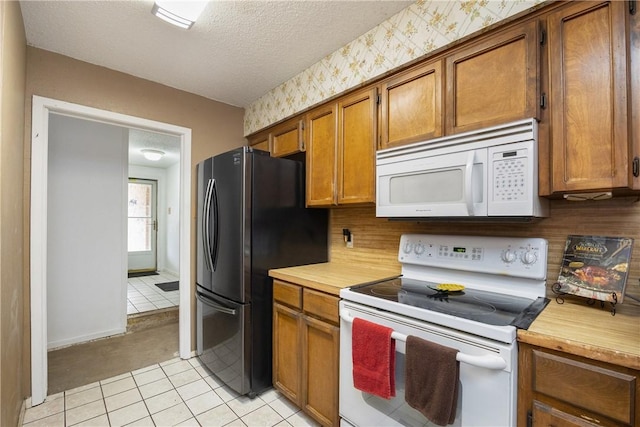 kitchen with brown cabinetry, a textured ceiling, white appliances, baseboards, and wallpapered walls