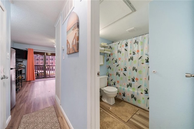 bathroom featuring a textured ceiling, hardwood / wood-style flooring, toilet, and shower / tub combo with curtain