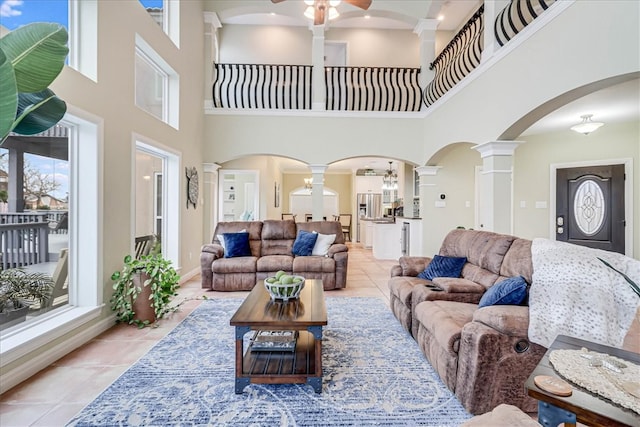 living room featuring a towering ceiling, ceiling fan, light tile patterned floors, and ornate columns