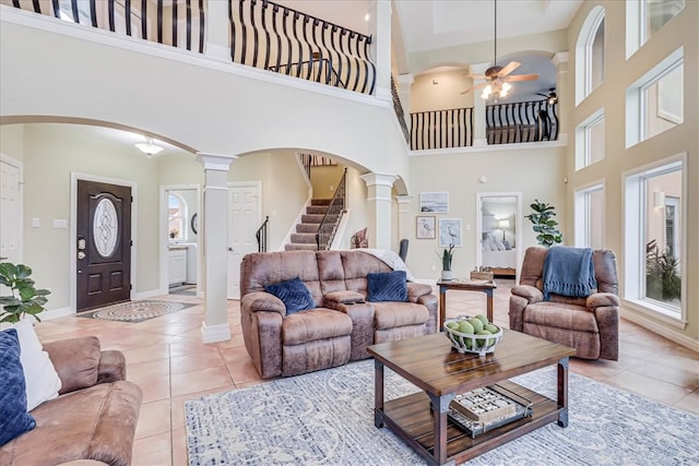 tiled living room featuring decorative columns, ceiling fan, and a towering ceiling