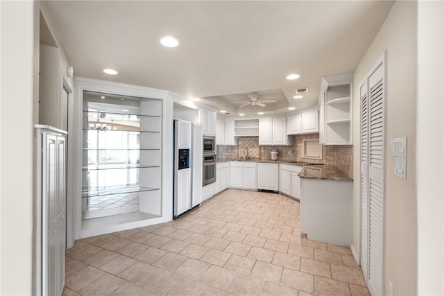 kitchen featuring white cabinetry, tasteful backsplash, built in appliances, ceiling fan, and dark stone counters