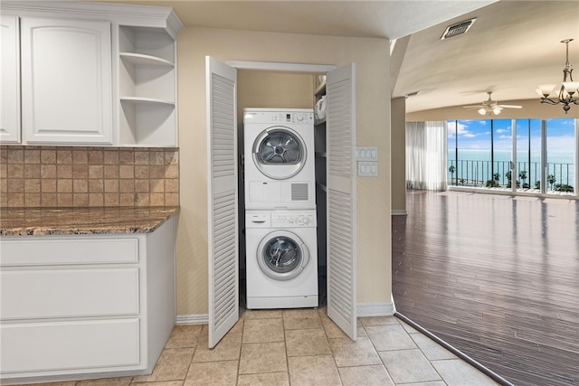 washroom with ceiling fan with notable chandelier, stacked washer and clothes dryer, and light tile patterned flooring