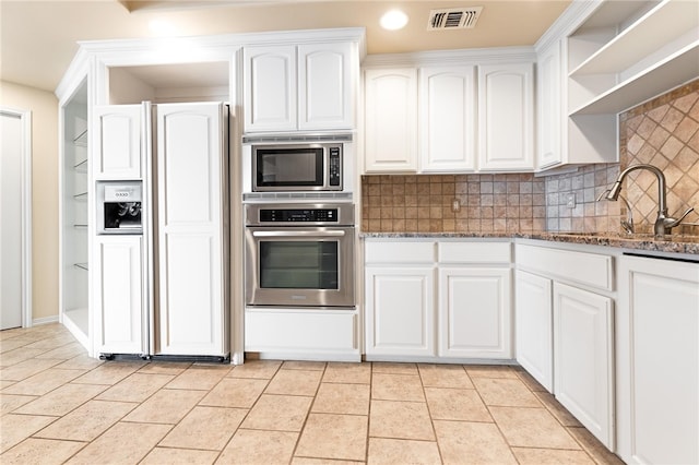 kitchen featuring dark stone counters, built in appliances, sink, and white cabinets