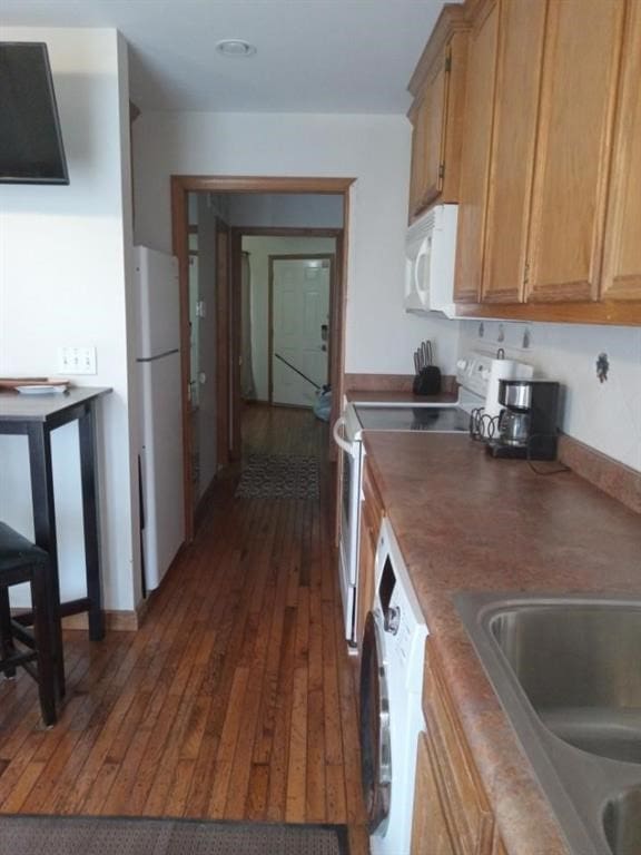 kitchen featuring white appliances, dark hardwood / wood-style floors, washer / dryer, and sink