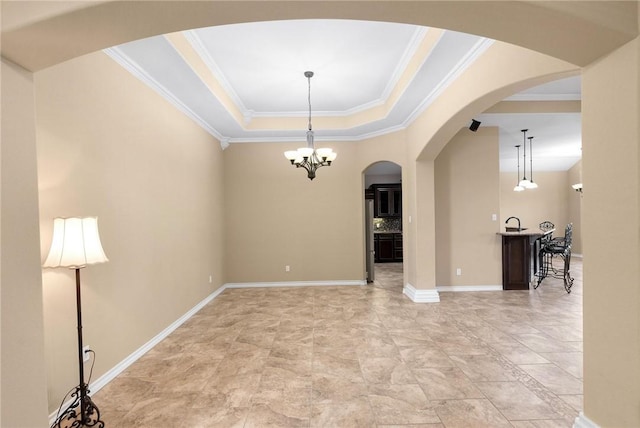 spare room with a notable chandelier, a raised ceiling, baseboards, and ornamental molding