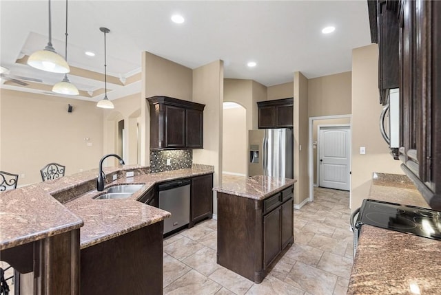 kitchen with sink, appliances with stainless steel finishes, a center island, light stone counters, and decorative light fixtures