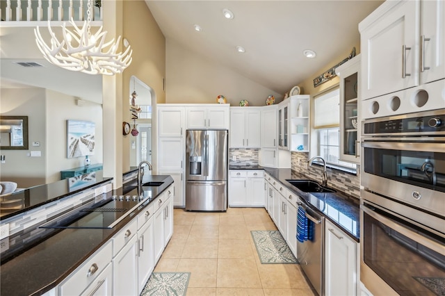 kitchen with lofted ceiling, white cabinets, sink, appliances with stainless steel finishes, and decorative light fixtures