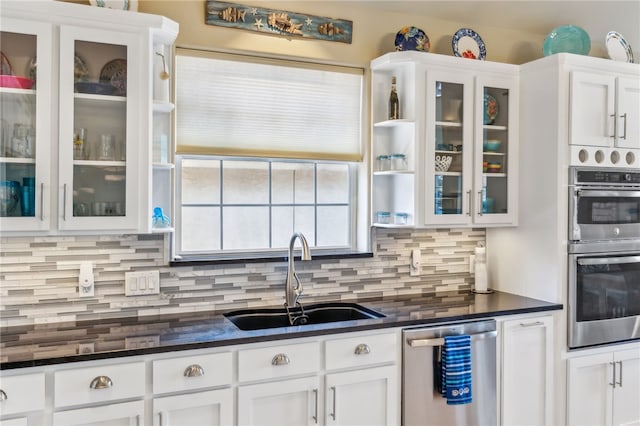 kitchen featuring dark stone counters, appliances with stainless steel finishes, decorative backsplash, sink, and white cabinets