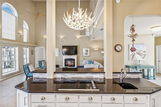 kitchen with white cabinetry, dark stone countertops, light tile patterned floors, decorative light fixtures, and a towering ceiling