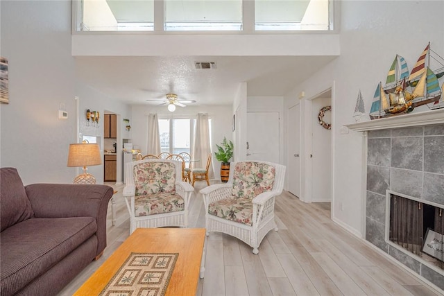 living room featuring light wood finished floors, visible vents, a tiled fireplace, a ceiling fan, and baseboards