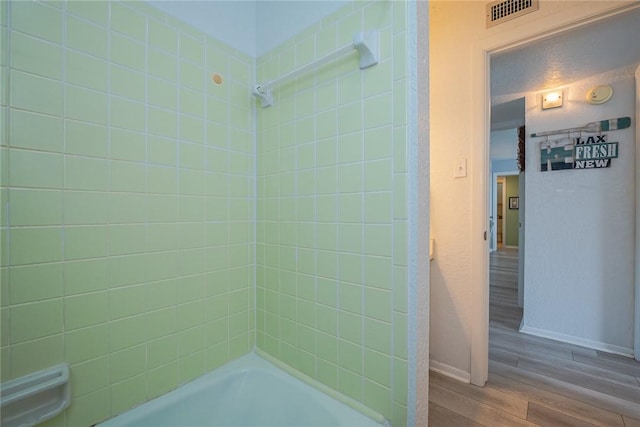 full bathroom featuring a textured ceiling, wood finished floors, visible vents, baseboards, and tub / shower combination