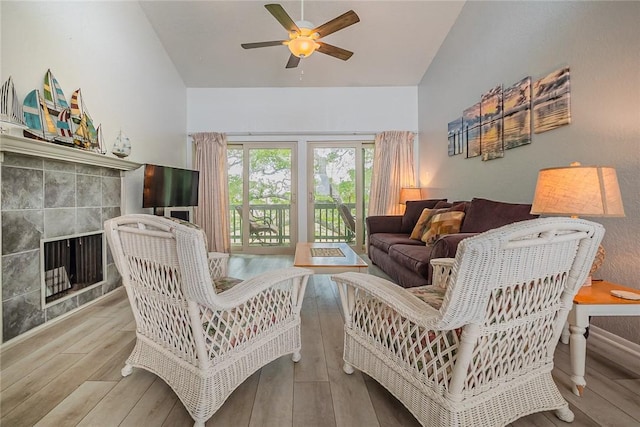 living area with ceiling fan, high vaulted ceiling, wood finished floors, and a tile fireplace