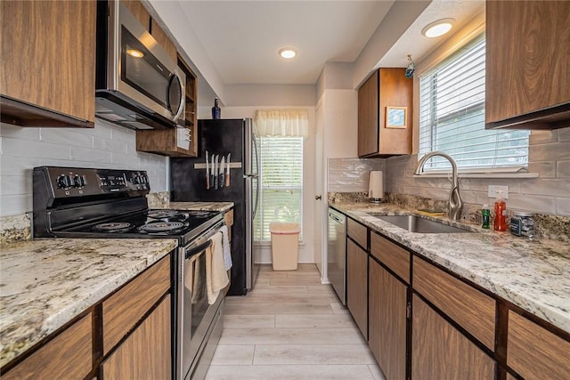 kitchen featuring appliances with stainless steel finishes, brown cabinets, a sink, and light stone countertops