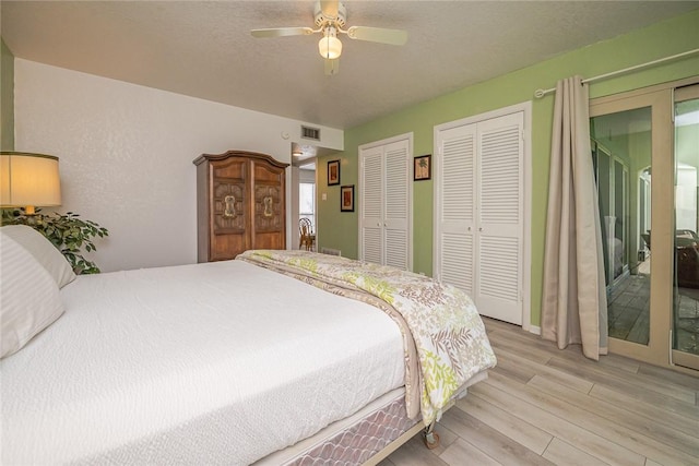 bedroom with visible vents, light wood-style flooring, ceiling fan, a textured ceiling, and two closets