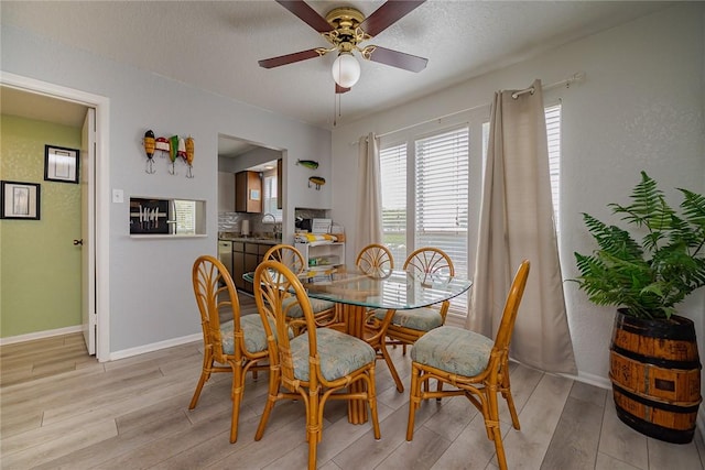 dining space with ceiling fan, light wood finished floors, a textured ceiling, and baseboards