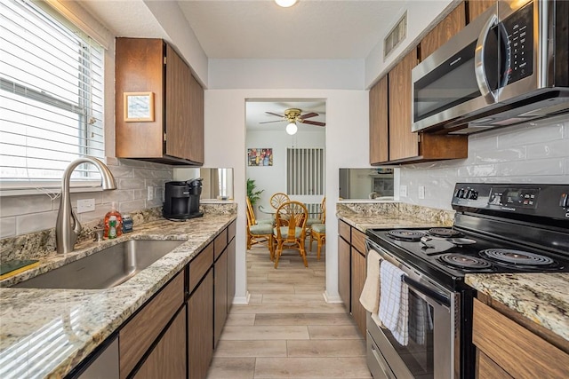 kitchen with appliances with stainless steel finishes, brown cabinetry, a sink, and visible vents