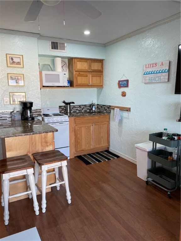 kitchen with dark stone counters, ornamental molding, dark hardwood / wood-style floors, ceiling fan, and white appliances