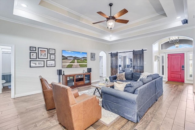 living room with a raised ceiling, a barn door, crown molding, and light hardwood / wood-style flooring