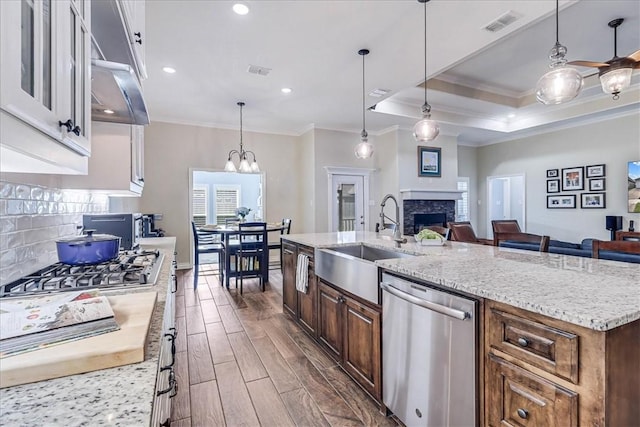 kitchen with light stone countertops, hanging light fixtures, stainless steel appliances, an island with sink, and ornamental molding