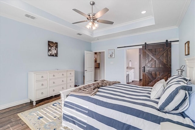 bedroom with ensuite bath, a raised ceiling, ceiling fan, a barn door, and dark hardwood / wood-style floors