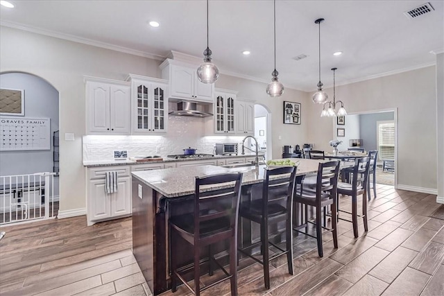 kitchen with decorative light fixtures, light stone counters, white cabinetry, and an island with sink