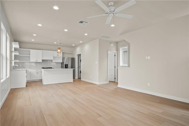 kitchen featuring visible vents, open shelves, stainless steel fridge with ice dispenser, stacked washer and dryer, and open floor plan