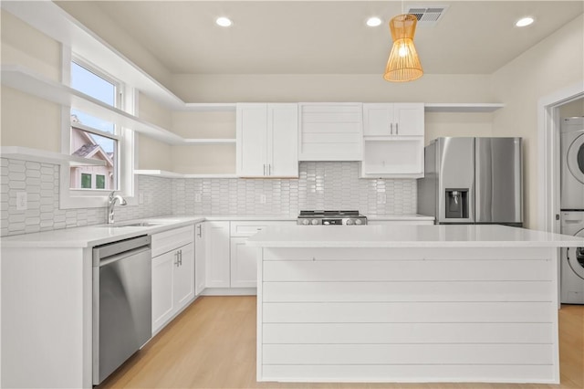 kitchen featuring visible vents, open shelves, a sink, stainless steel appliances, and stacked washer and clothes dryer