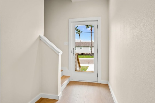 doorway featuring baseboards, light wood-style flooring, and stairs