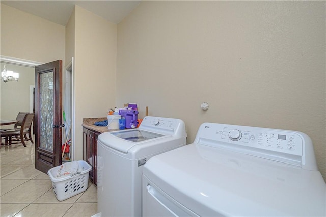 clothes washing area with light tile patterned floors, a chandelier, washer and dryer, and cabinet space