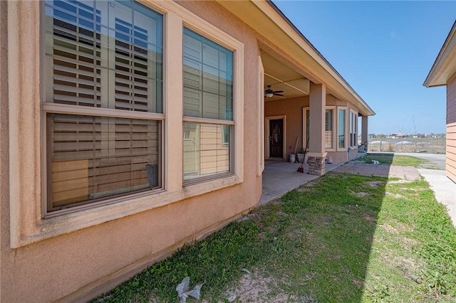 exterior space featuring stucco siding, a lawn, and ceiling fan