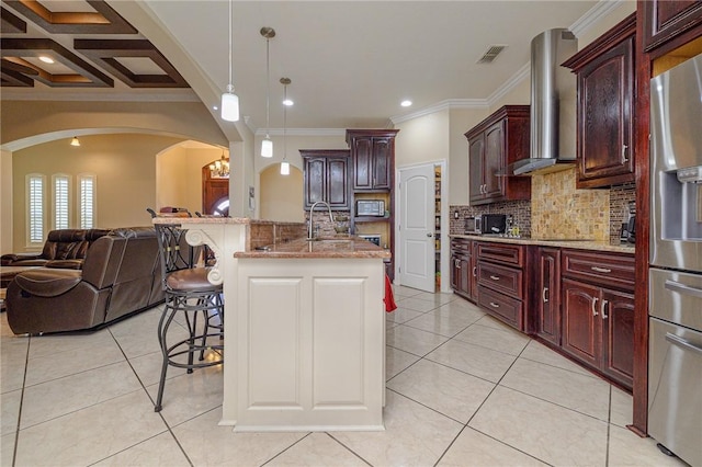 kitchen featuring visible vents, arched walkways, a kitchen bar, wall chimney range hood, and open floor plan