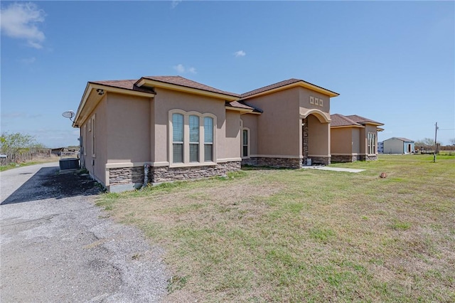 rear view of house with stucco siding, stone siding, and a yard