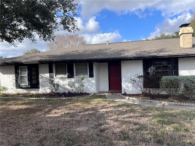 ranch-style home with roof with shingles, brick siding, a front lawn, and a chimney