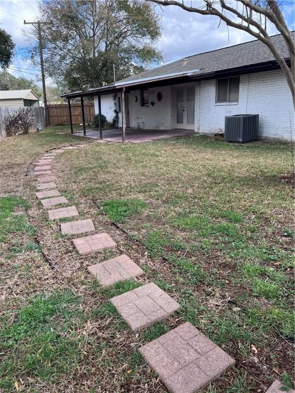 exterior space with roof with shingles, brick siding, a yard, central air condition unit, and fence