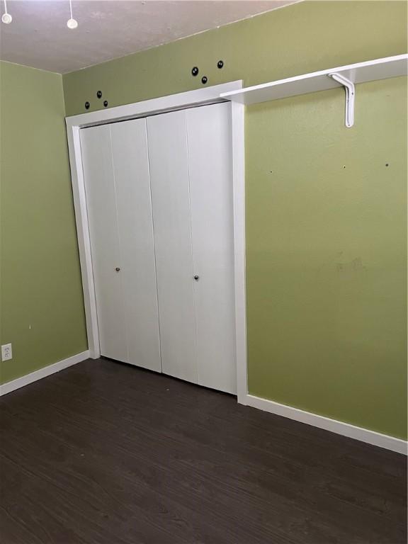 unfurnished bedroom featuring dark wood-style flooring, a closet, and baseboards