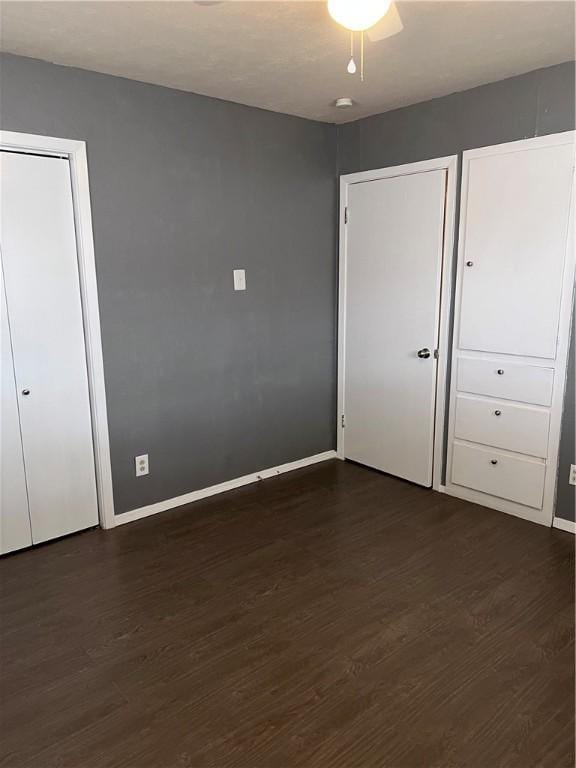 unfurnished bedroom featuring dark wood-style flooring, a ceiling fan, and baseboards