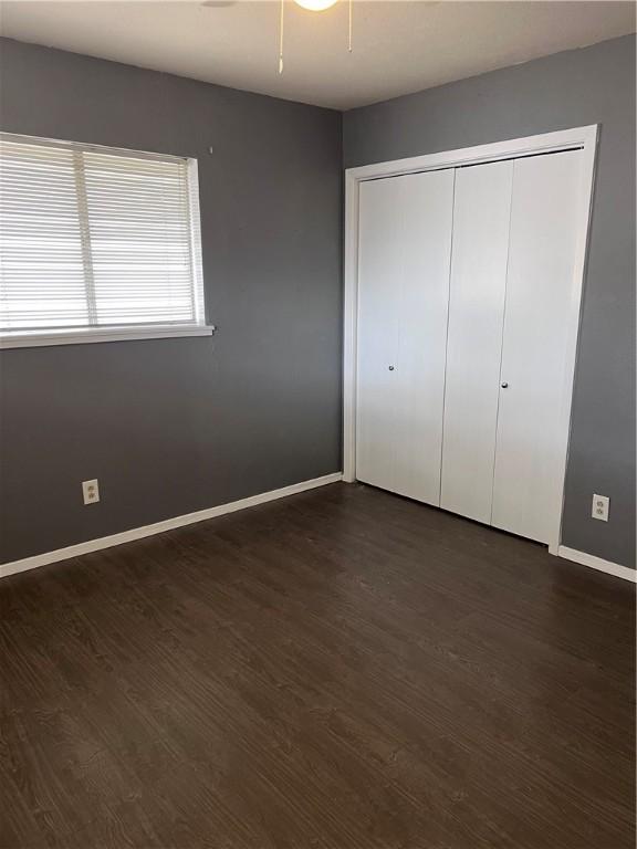 unfurnished bedroom featuring ceiling fan, a closet, baseboards, and dark wood-style flooring