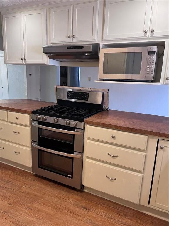 kitchen featuring under cabinet range hood, butcher block countertops, white cabinetry, appliances with stainless steel finishes, and light wood-type flooring