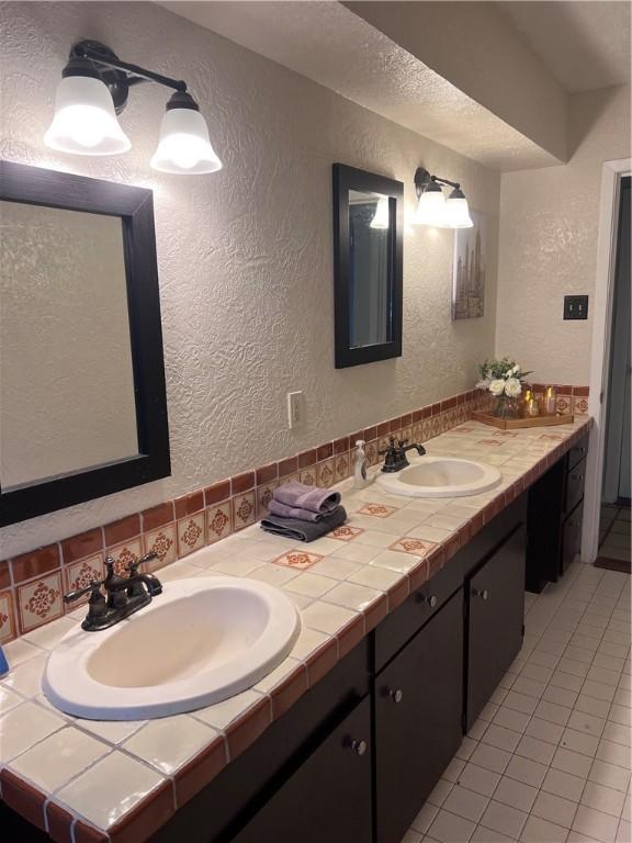 bathroom featuring a textured wall, double vanity, and a sink