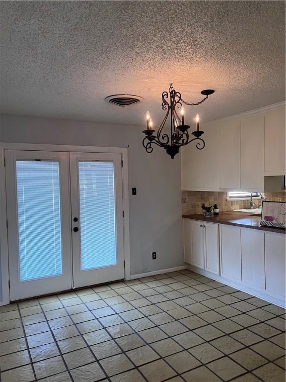 unfurnished dining area with french doors, visible vents, an inviting chandelier, a textured ceiling, and baseboards