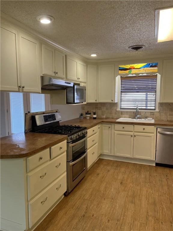 kitchen with under cabinet range hood, a sink, wood counters, light wood-style floors, and appliances with stainless steel finishes